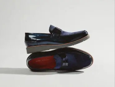 Pair of navy blue patent leather and suede loafers with orange trim and a stacked sole, one shoe resting on top of the other.