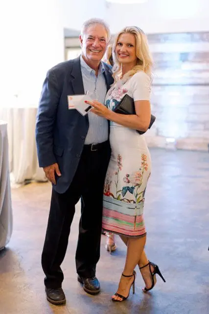 Man in a navy blazer and woman in a floral dress smiling at an event.