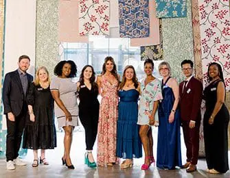 Group of ten people, five men and five women, standing in front of a wall displaying various fabric and wallpaper samples.