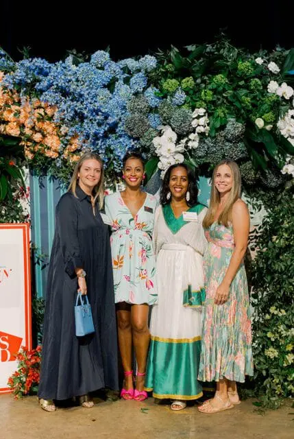 Four women standing in front of a floral backdrop.