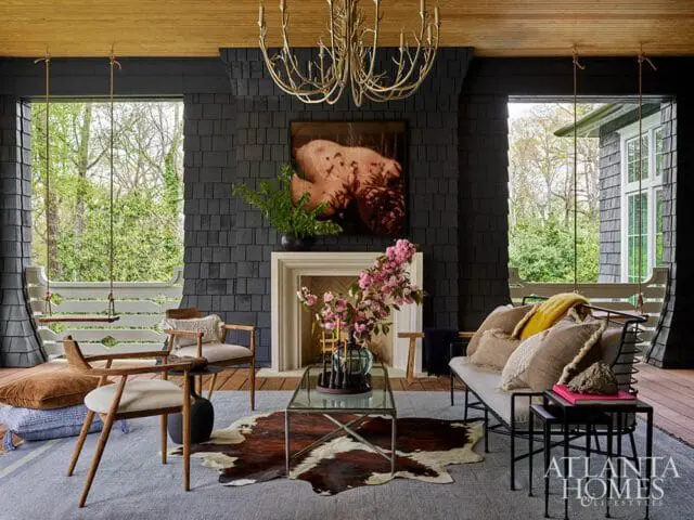Living room with dark gray shingle walls, a white fireplace, wooden chairs, a sofa with textured pillows, and two swings hanging from the ceiling.