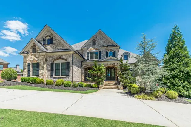 Luxury brick and stone home with multiple gables, arched windows, black shutters, and a covered entryway with stone steps.