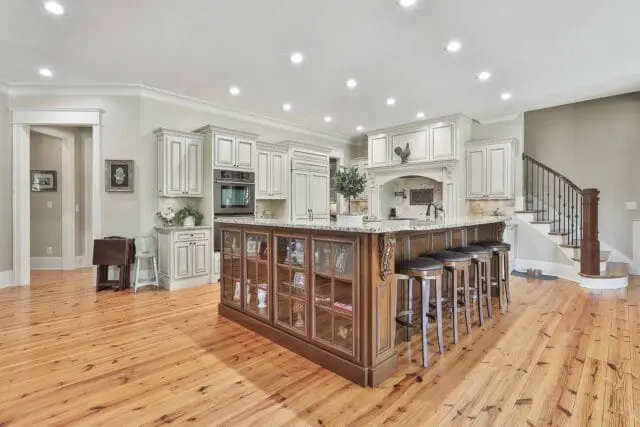 Cream kitchen with white paneled cabinetry, granite countertops, and a large wooden island with glass display cabinets and bar stools.