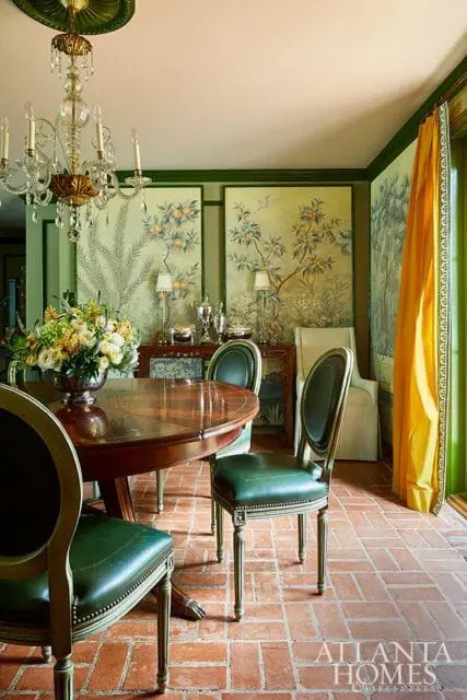 Dining room with a round wooden table, green leather chairs, chinoiserie wallpaper, and a crystal chandelier.