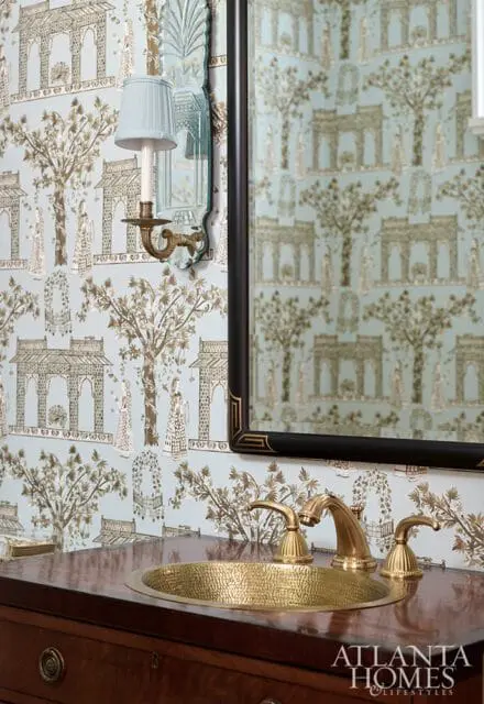 Powder room with light blue chinoiserie wallpaper, brass faucet and hammered brass sink set in a dark wood vanity.