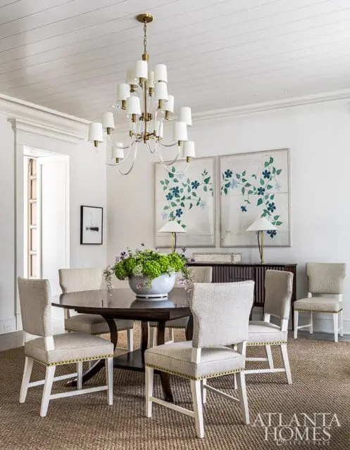 Dining room with dark wood table, upholstered chairs with gold nailhead trim, floral artwork, and brass chandelier.