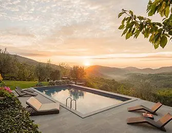 Rectangular swimming pool with lounge chairs on stone patio overlooking rolling hills at sunset