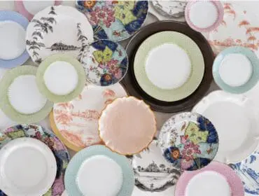 Assortment of decorative plates with various patterns including floral, landscape scenes, and geometric borders in pink, blue, green, and white.