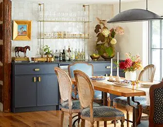 Dining room with dark blue cabinets, brass shelving, and a wooden table set for a meal.