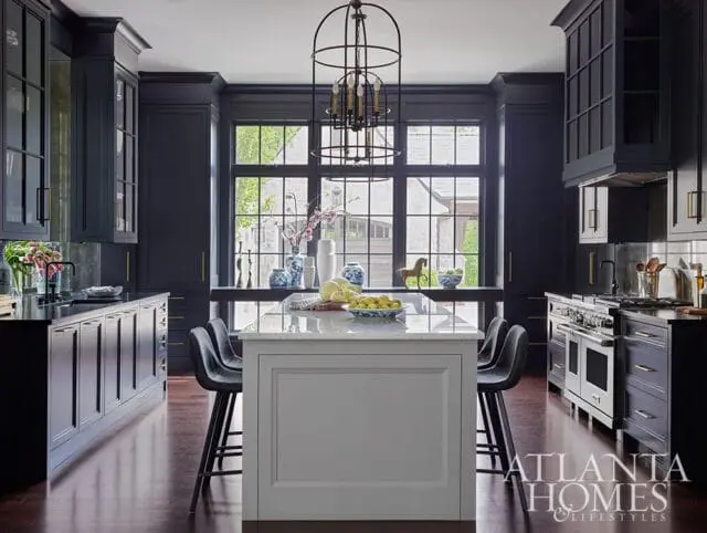 Dark blue kitchen with a white marble island, stainless steel range, and large windows overlooking a garden.