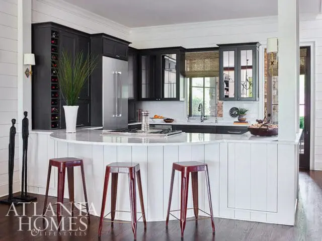 Dark gray kitchen island with marble countertop, stainless steel appliances, and wine rack. Three red metal stools are in front of the island.