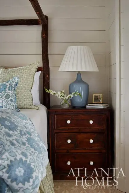 Bedroom with a rustic log canopy bed, blue floral bedding, and a dark wood nightstand with a blue lamp and white pleated shade.