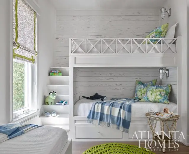 Children's bedroom with white bunk beds, white shiplap walls, green and blue patterned pillows, and a white quilted bed.