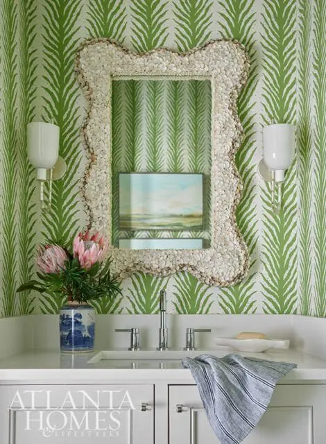 Powder room with green palm leaf wallpaper, a shell-encrusted mirror, and a white vanity with a silver faucet.