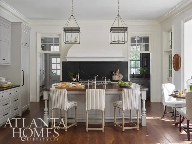 Kitchen with white custom cabinetry, a large island with a wooden countertop, striped bar stools, and black marble backsplash.