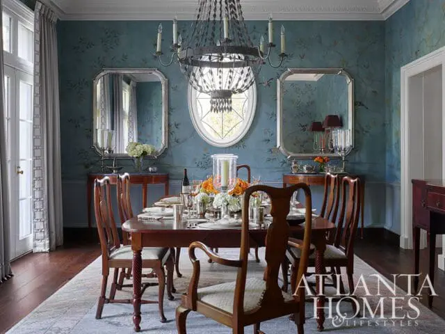 Formal dining room with a dark wood table set for a meal, upholstered chairs, ornate mirrors, and blue chinoiserie wallpaper.