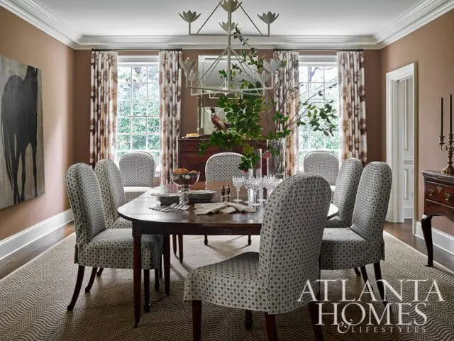 Dining room with a dark wood oval table surrounded by upholstered chairs with a black and white geometric pattern. A large abstract painting hangs on the brown wall.