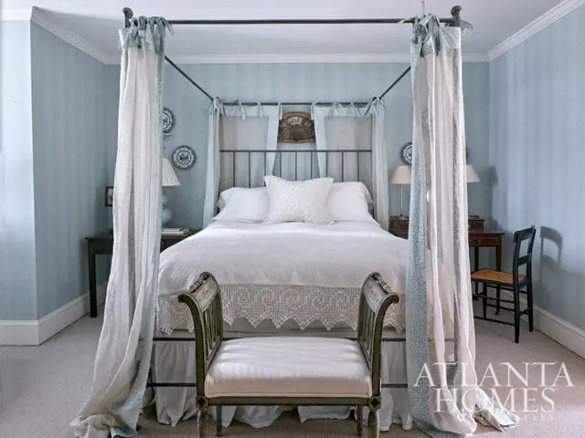 Bedroom with a four-poster bed draped in white and blue floral curtains, light blue textured wallpaper, and a white upholstered bench.