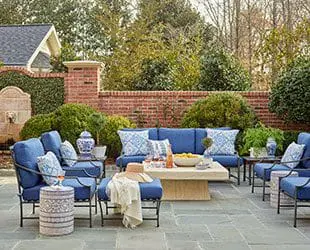 Patio with blue upholstered furniture, brick wall, and lush greenery