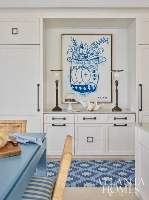 White kitchen with blue and white abstract art, two glass lamps, and a blue geometric rug. A blue table and chairs are in the foreground.