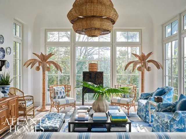 Living room with rattan furniture, blue and white patterned upholstery, large wicker chandelier, and decorative palm trees.