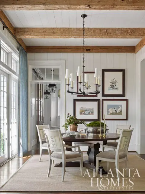 Dining room with white paneled walls, exposed wooden beams, round dark wood table with four chairs, and artwork of birds on the wall.