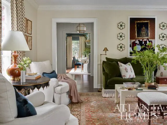 Living room with a green velvet sofa, white armchairs, a patterned rug, and a view into a dining room.