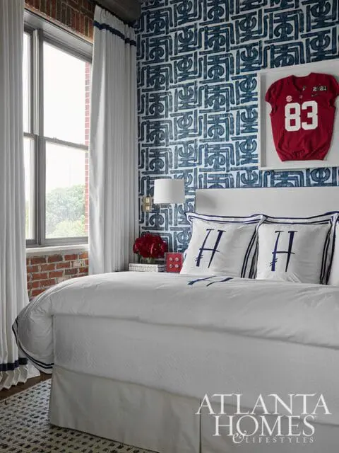 Bedroom with white bedding, navy and white patterned wallpaper, and a framed red football jersey with the number 83.