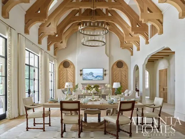 Great room with vaulted wooden beamed ceiling, large windows with cream curtains, and a dining table set for a meal.