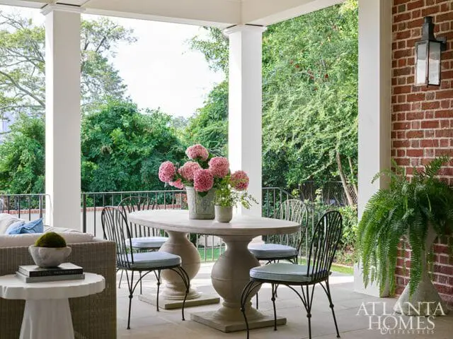 Covered patio with stone table and chairs, pink hydrangeas, and lush green trees in the background.