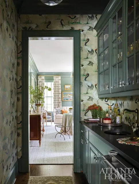 Hallway with crane-patterned wallpaper and a dark countertop wet bar with glass-front cabinets. A doorway opens to a living area with a sofa and table.
