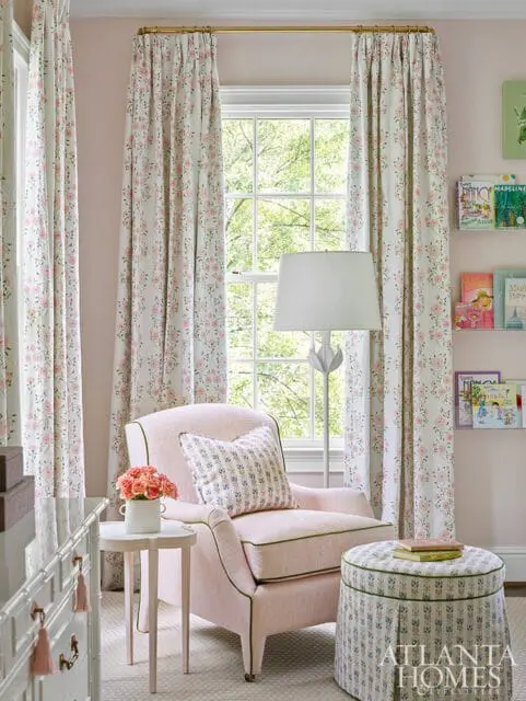 Pink armchair with floral patterned curtains, a small side table with roses, and a bookshelf filled with children's books.