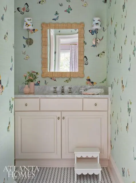 Powder room with light green butterfly wallpaper, a marble vanity with a rattan mirror, and a cream-colored cabinet.