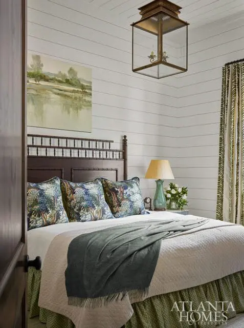 Bedroom with shiplap walls, dark wood headboard, quilted bedspread, forest-themed pillows, and a brass lantern pendant light.