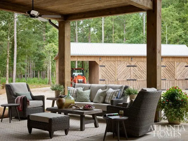 Covered porch with wicker seating, wooden beams, and a view of a barn with an orange tractor.