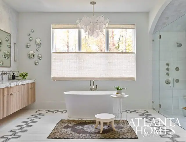 Modern bathroom with freestanding white tub, glass-enclosed shower, wood-paneled vanity with marble countertop, and decorative floor tile.