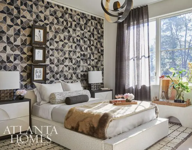 Bedroom with a geometric patterned wallpaper, a white bed with a faux fur throw, and a large window with sheer curtains.