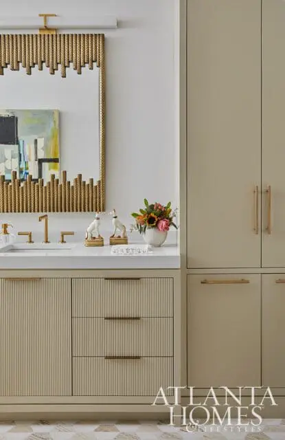 Modern bathroom vanity with fluted beige cabinetry, white countertop, gold faucet, and a decorative mirror with gold accents.