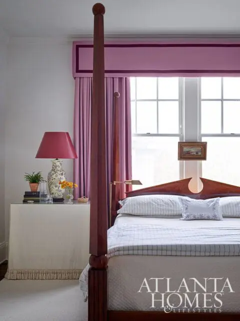 Bedroom with a mahogany four-poster bed, white bedding with pinstripe accents, and a pink upholstered valance with purple trim over pink curtains.
