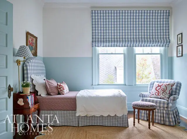 Bedroom with light blue and white walls, featuring a twin bed with a blue gingham headboard and bed skirt, a patterned duvet, and a blue gingham armchair with a matching ottoman.