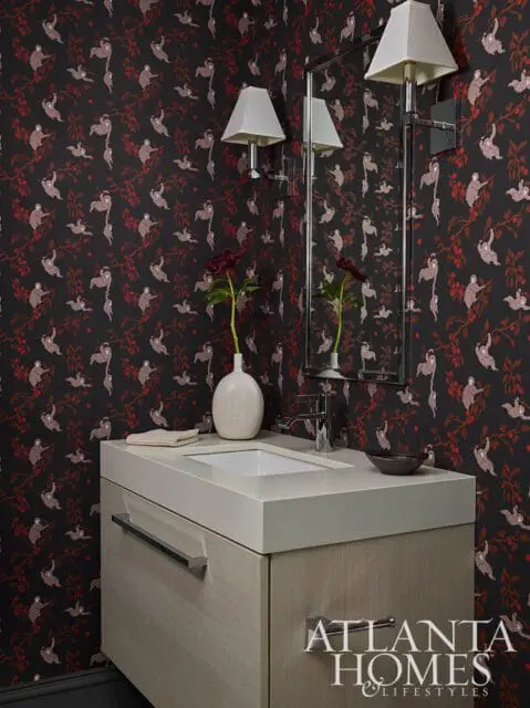 Powder room with dark floral wallpaper featuring sloths, a light wood vanity with a white countertop and sink, and two wall-mounted sconces.