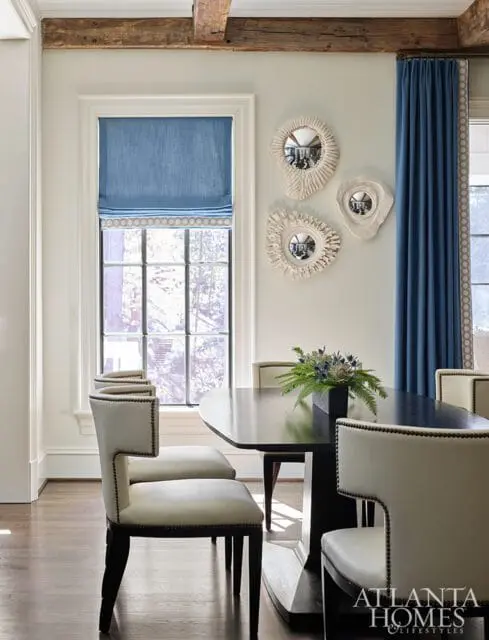 Dining room with a dark wood table, upholstered chairs with nailhead trim, blue Roman shades, and decorative shell-like mirrors on the wall.