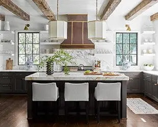 Kitchen with dark cabinets, marble island, pendant lights, and exposed 
  beams