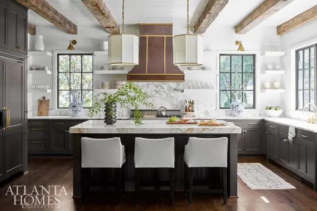 Dark gray kitchen with marble island and countertops, white octagonal pendant lights, and exposed wooden ceiling beams.