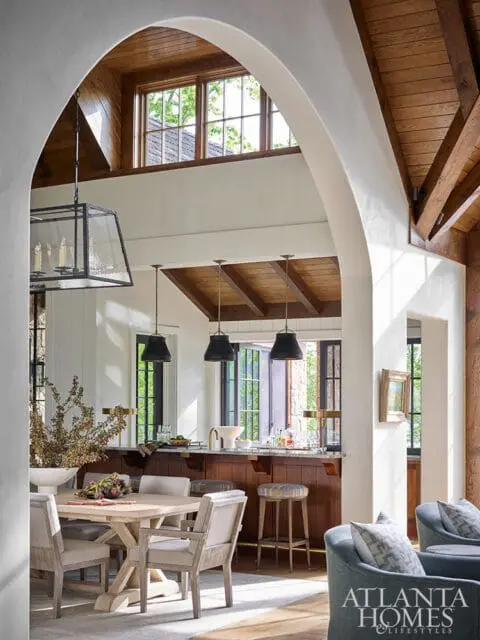 Dining area with light wood table and upholstered chairs, adjacent to a wood bar with pendant lights and stools.