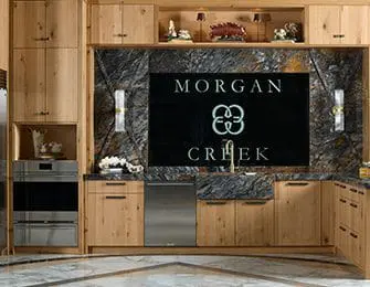 Light wood cabinetry with a black marble backsplash featuring the 'Morgan Creek' logo. Includes stainless steel appliances and modern lighting.