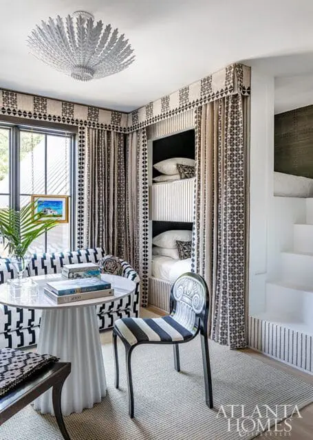 Monochromatic patterned room with built-in bunk beds, a round white table with books, and a striped chair.