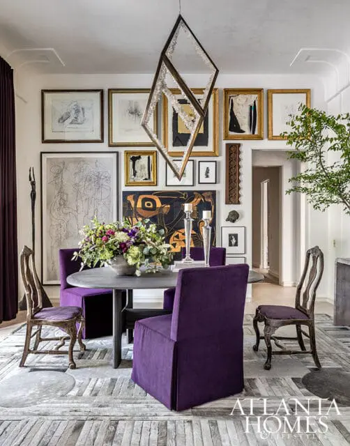Dining room with purple upholstered chairs around a dark wood table, eclectic artwork on the walls, and a geometric crystal chandelier.