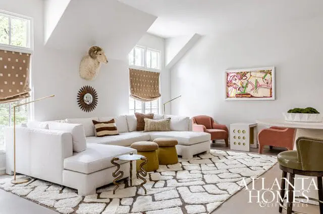 Living room with a large white sectional sofa, two coral armchairs, a taxidermy ram head, and abstract art on the wall.