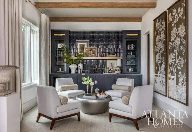 Living room with four light gray armchairs arranged around a silver coffee table, facing a dark gray built-in bar with black tile backsplash and gold accents.